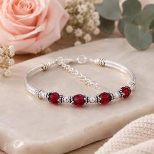 May include: Silver bracelet with five faceted, deep red beads. The bracelet has a delicate design with small silver beads between the red beads. The clasp is adjustable. A beautiful piece of jewelry.