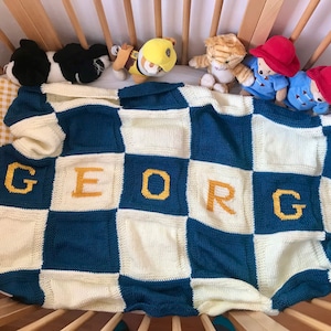 Może przedstawiać: Niebiesko-biały, kratkowany, dziergany kocyk dla dziecka z imieniem "GEORGE" wyszytym żółtą nicią.