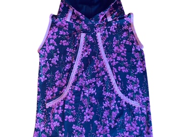 Puede incluir: Vestido sin mangas con capucha y estampado floral en tonos rosa y morado sobre fondo azul oscuro. El vestido tiene un ribete rosa alrededor de la capucha y el escote.
