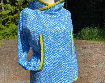 Puede incluir: Una sudadera con capucha azul con un estampado floral blanco. El forro y el ribete de la capucha son amarillos, y los bolsillos tienen ribetes verdes. La sudadera se exhibe en un maniquí al aire libre.