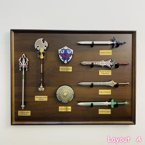 Puede incluir: Un expositor de madera con una colección de espadas, escudos y una lanza. Los artículos incluyen la Espada Maestra, el Escudo Hyliano y la Espada de la Diosa. El texto "Layout A" es visible en la parte inferior.