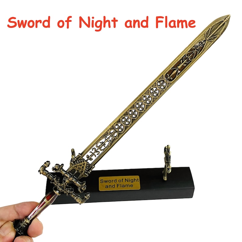 Op de afbeelding: Een sierlijk bronzen zwaard met een decoratief handvat en lemmet, rustend op een zwarte standaard. Het zwaard heeft ingewikkelde patronen en de tekst "Sword of Night and Flame" is zichtbaar.