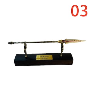 May include: A decorative spear, the Draupnir Spear, is displayed on a black wooden base. The spear features a gold-colored blade with red accents and a detailed handle. The number "03" is in the upper right corner.
