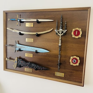 Op de afbeelding: Een houten display met verschillende zwaarden en een speer. De zwaarden zijn onder meer het Carian Knight's Sword, Malenia's Freehand Sword, Holy Moonlight Sword en Maliketh's Black Blade. De speer is Mohgwyn's Sacred Spear.