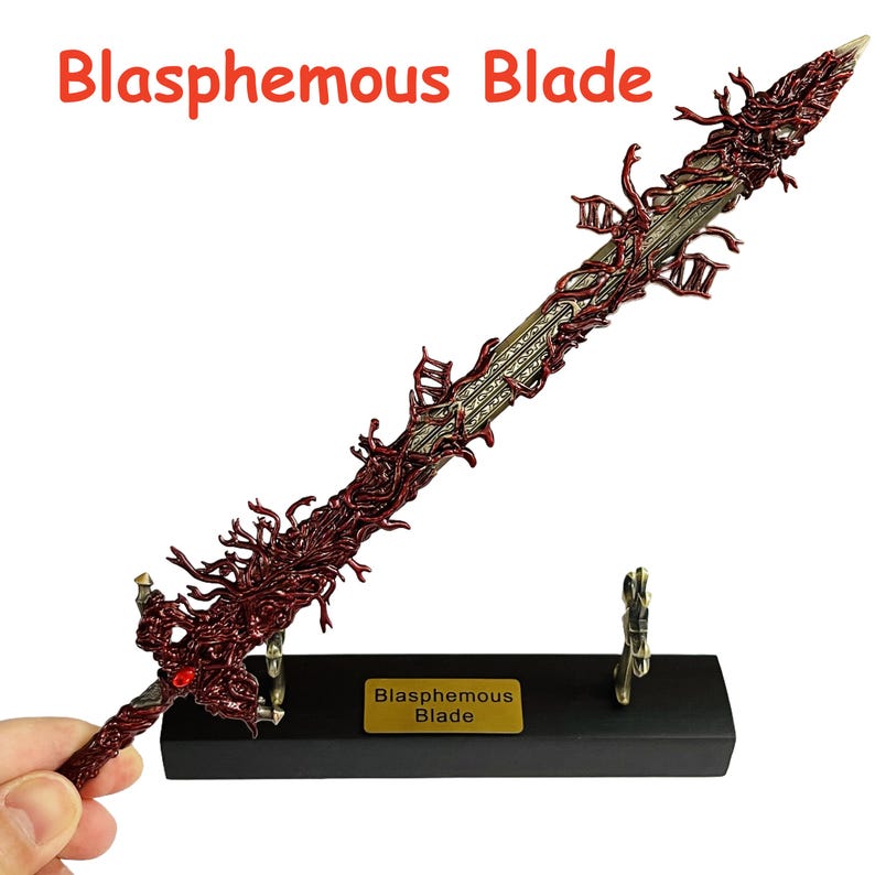 Op de afbeelding: Een gedetailleerd, versierd zwaard met een rood en goud kleurenschema, met ingewikkelde, wijnstokachtige details langs het lemmet en de handgreep. De tekst "Blasphemous Blade" is zichtbaar boven het zwaard. Het zwaard rust op een zwarte standaard met een gouden naamplaatje.