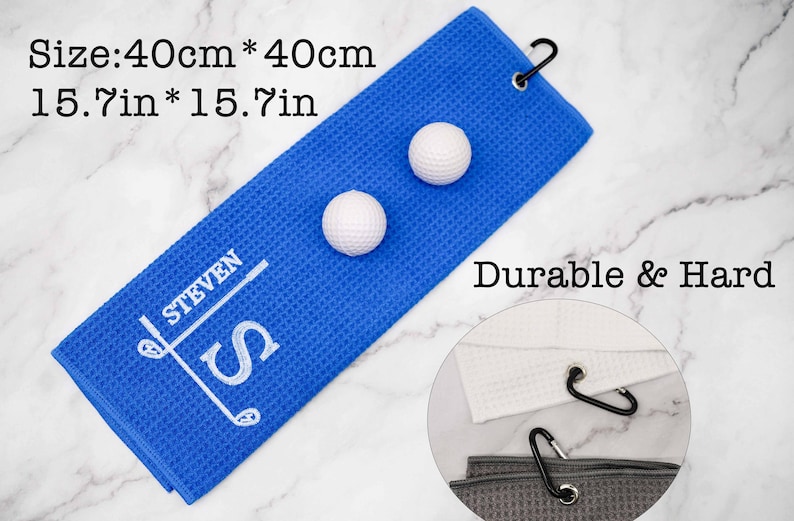 Puede incluir: Toalla de golf azul con el texto "STEVEN" bordado en blanco y un dise&ntilde;o de palo de golf. La toalla mide 40 cm por 40 cm y tiene dos bolas de golf blancas en la parte superior. El texto "Durable & Hard" es visible en el fondo.