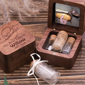 May include: A wooden pet memorial box with a hinged lid, engraved with "My Best Friend Willow 2012-2024" and a dog silhouette. Inside, there's a photo and small glass vials. A separate vial is tied with a white ribbon.