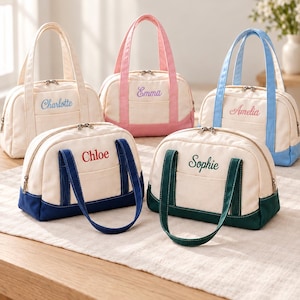 May include: Five canvas handbags with top handles and zippered closures. Each bag features a cream-coloured body with a coloured base and matching handles in pink, light blue, dark blue, dark green, or cream. Names are embroidered on the front.
