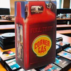 May include: A red gas can with the words "Full Tank" and "Corner Gas" printed on it. The gas can is a DVD box set for the TV show "Corner Gas".