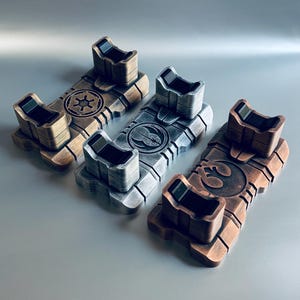 May include: Three metallic-toned display stands, each featuring a unique emblem. The stands are rectangular with a raised platform and two upright supports. The emblems include a star, a bird, and a circular design. The stands are in shades of bronze, silver, and copper.