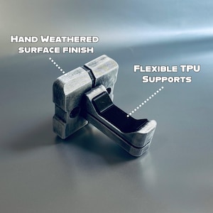 May include: A grey, rectangular object with a hand-weathered surface finish and flexible TPU supports. The text "HAND WEATHERED SURFACE FINISH" and "FLEXIBLE TPU SUPPORTS" are visible. The object is designed to hold something.