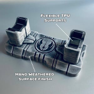 May include: A weathered gray TPU stand with flexible supports, featuring a hand-weathered surface finish. The stand has a symbol in the center and text that reads "FLEXIBLE TPU SUPPORTS" and "HAND WEATHERED SURFACE FINISH".