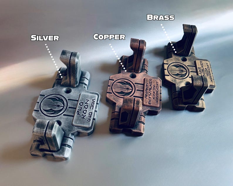 May include: Three rectangular wall mounts in silver, copper, and brass finishes. Each mount features two vertical prongs, a circular Jedi Order emblem, and engraved text reading Plo Koon, Anakin Skywalker, or Luke Skywalker in English and Aurebesh.