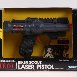 May include: A Star Wars Biker Scout Laser Pistol toy in its original packaging. The black and gray pistol has a red trigger and is packaged in a black box with yellow interior. The box features the text "Star Wars Return of the Jedi".