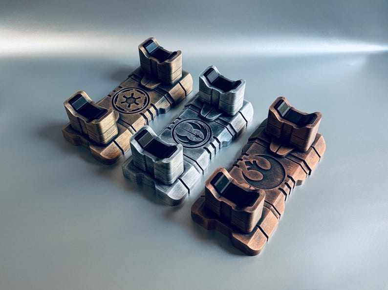 May include: Three metallic-toned display stands, each featuring a unique emblem. The stands are rectangular with a raised platform and two upright supports. The emblems include a star, a bird, and a circular design. The stands are in shades of bronze, silver, and copper.