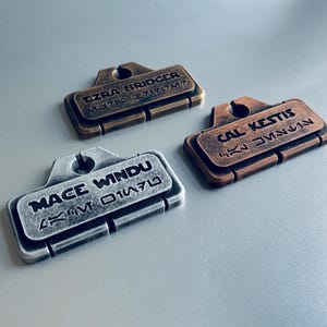 May include: Three metal name tags with different names and unique lettering styles. The tags are silver, bronze, and copper in color.