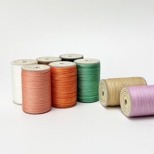 May include: Eight spools of waxed thread in various colours, including white, peach, orange, green, beige, and lavender. The spools are arranged in a row on a white surface.