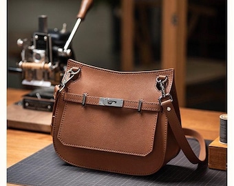 May include: A brown leather crossbody bag with a flap closure and silver-tone hardware. The bag has a long adjustable strap and a front pocket. The bag is sitting on a black surface.