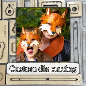 Puede incluir: Dos personas con máscaras de zorro naranjas y blancas. Las máscaras tienen orejas puntiagudas y son de cuero. La imagen también muestra herramientas de corte de troqueles de madera y el texto "Custom die cutting".