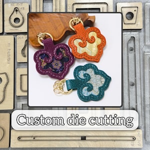 May include: Three decorative keychains in purple, orange, and teal, each with a unique design and gold-colored hardware. The keychains are cloud-shaped with intricate patterns. The image also includes the text "Custom die cutting".