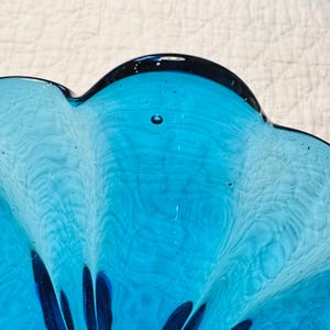 K&ouml;nnte beinhalten: Nahaufnahme einer t&uuml;rkisfarbenen Glasschale mit gewelltem Rand. Die Schale hat einen dunkelblauen Rand und sichtbare Blasen im Glas. Die Oberfl&auml;che der Schale hat eine wellenf&ouml;rmige Textur.