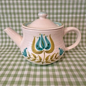 May include: A white ceramic teapot with a floral design in shades of blue, green, and yellow. The teapot has a lid and a handle.
