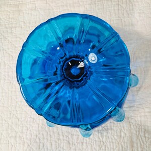 K&ouml;nnte beinhalten: Eine leuchtend blaue Glasschale mit einem einzigartigen, bl&uuml;tenartigen Design. Die Schale hat eine dunkle Mitte und eine strukturierte, geriffelte Au&szlig;enseite. Sie hat drei kleine, abgerundete F&uuml;&szlig;e und steht auf einem wei&szlig;en Hintergrund.