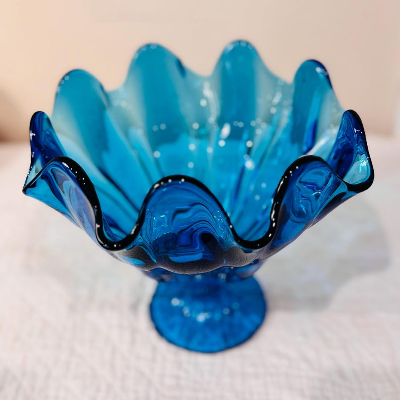 K&ouml;nnte beinhalten: Eine leuchtend blaue Glasschale mit gewelltem Rand und Sockel. Die R&auml;nder der Schale sind schwarz umrandet, und das Innere hat wei&szlig;e Sprenkel. Dieses dekorative St&uuml;ck ist ideal zum Servieren oder Ausstellen.