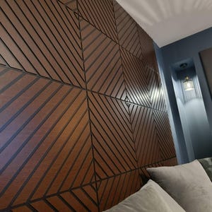 Könnte beinhalten: Nahaufnahme einer Holz-Wandverkleidung mit geometrischem Design. Die Paneele sind warmbraun mit dunkelbraunen Linien, die ein sich wiederholendes Muster aus diagonalen Linien und Rauten bilden. Die Wand befindet sich in einem Schlafzimmer.
