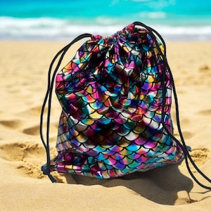 May include: A drawstring bag with a mermaid scale pattern in iridescent colors of pink, blue, green, and gold. The bag is made of a shiny, metallic fabric.