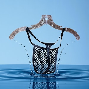 May include: A black mesh thong suspended from a clear plastic hanger. The thong is designed with a diamond-shaped pattern. Water droplets are splashing around the garment, set against a light blue background.