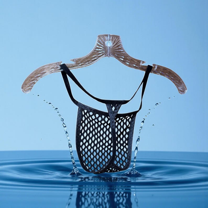 May include: A black mesh thong suspended from a clear plastic hanger. The thong is designed with a diamond-shaped pattern. Water droplets are splashing around the garment, set against a light blue background.