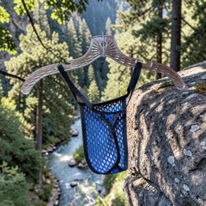 May include: A blue mesh pouch underwear with black trim, hanging from a clear plastic hanger. The background features a scenic view of a river and forest.