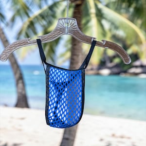 May include: A blue mesh bag with black trim hangs from a clear plastic hanger. The bag is suspended against a backdrop of a beach with palm trees and turquoise water.