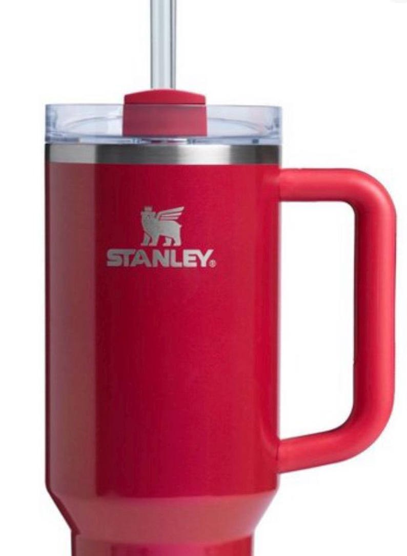 May include: A red stainless steel travel mug with a black handle and a black logo that says "STANLEY". The mug has a clear lid with a red straw.