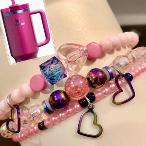 May include: A set of four pink and iridescent bracelets with heart charms. The bracelets feature pink beads, clear beads, and iridescent beads. The heart charms are made of metal and have a rainbow finish.