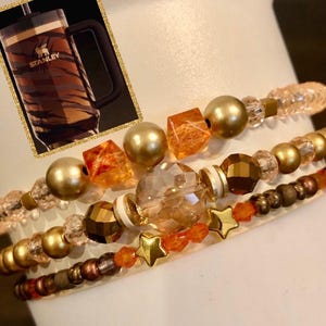 May include: A set of four bracelets featuring gold, orange, and clear beads. The bracelets are stacked on top of each other and have a variety of different bead shapes and sizes.