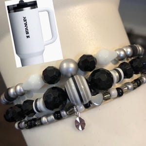May include: A set of four black and white beaded bracelets with a silver charm. The bracelets feature different sized beads, including round, faceted, and striped beads.