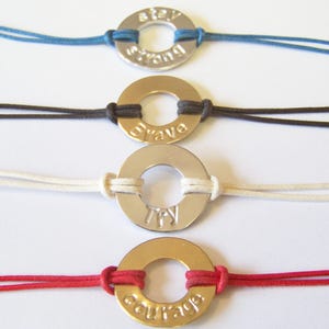 May include: Four bracelets with different colored cords and metal rings with inspirational words engraved on them. The words are "stay strong", "brave", "try", and "courage".