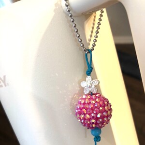 May include: A pink sparkly ball charm with a silver flower charm and a turquoise bead on a silver chain.