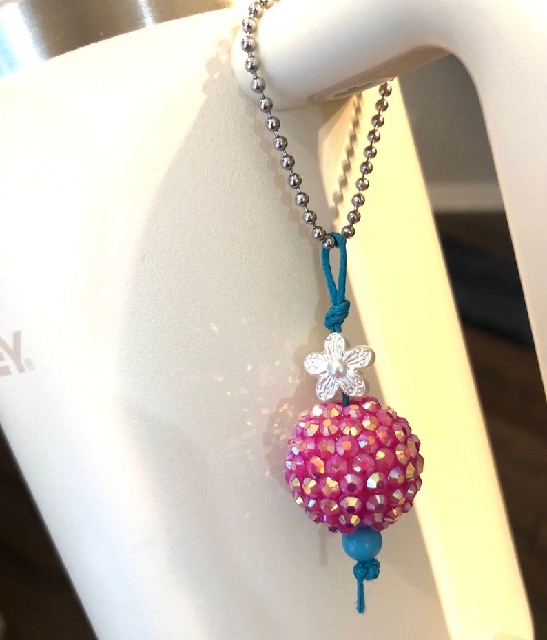 May include: A pink sparkly ball charm with a silver flower charm and a turquoise bead on a silver chain.