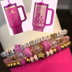 Pu&ograve; includere: Due bicchieri in acciaio inossidabile rosa con dettagli dorati e una cannuccia. Un bicchiere ha la scritta "Barbie" e l'altro la scritta "Stanley". Un braccialetto rosa e oro con la scritta "Barbie Girl".