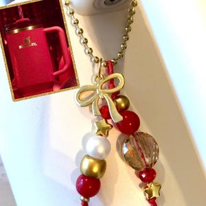 May include: A gold chain necklace with a gold bow charm and red and gold beads. The beads are strung on red string and include a clear crystal bead, a white pearl bead, and gold star charms.