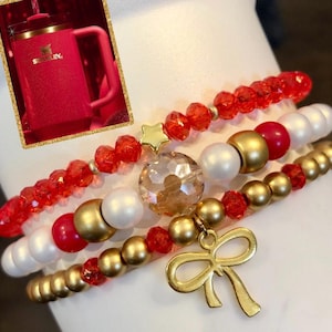 May include: Four layered bracelets with red and gold beads, white pearls, a gold star charm, a large clear crystal bead, and a gold bow charm.