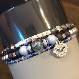 May include: A set of four bracelets with silver, blue, and iridescent beads. The bracelets are stacked on top of each other and have a silver charm in the shape of lips.