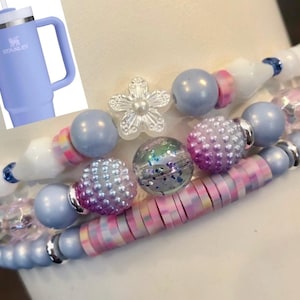 May include: A set of four bracelets with blue, white, pink, and iridescent beads. The bracelets are stacked on top of each other and feature a variety of different bead shapes and sizes.