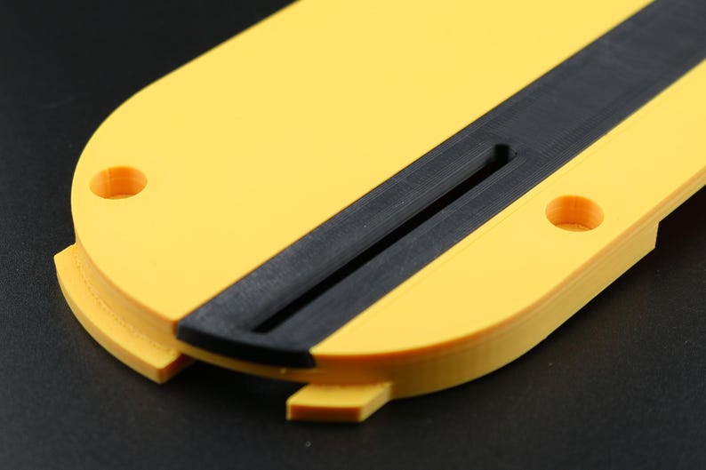 May include: A yellow and black 3D-printed object with a rounded shape. The object has a black stripe down the center and two circular holes. The object is likely a component or part of a larger item.