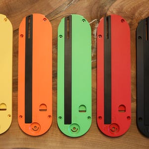 May include: Five colorful, elongated, rectangular objects in yellow, orange, green, red, and black. Each has a black stripe down the center and a circular opening at the bottom. The objects are arranged vertically on a wooden surface.
