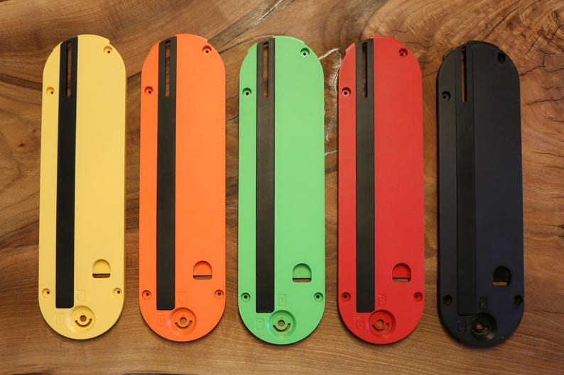 May include: Five colorful, elongated, rectangular objects in yellow, orange, green, red, and black. Each has a black stripe down the center and a circular opening at the bottom. The objects are arranged vertically on a wooden surface.