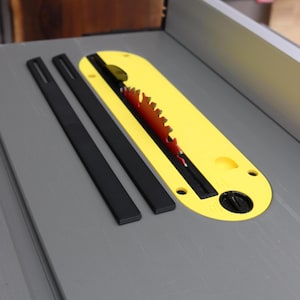 May include: A yellow table saw blade guard with a red blade and two black blade inserts. The guard has a slot for the blade and several mounting holes. The blade is circular with sharp teeth.